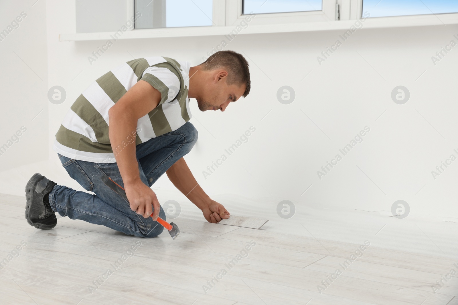 Photo of Professional worker using hammer during installation of new laminate flooring indoors