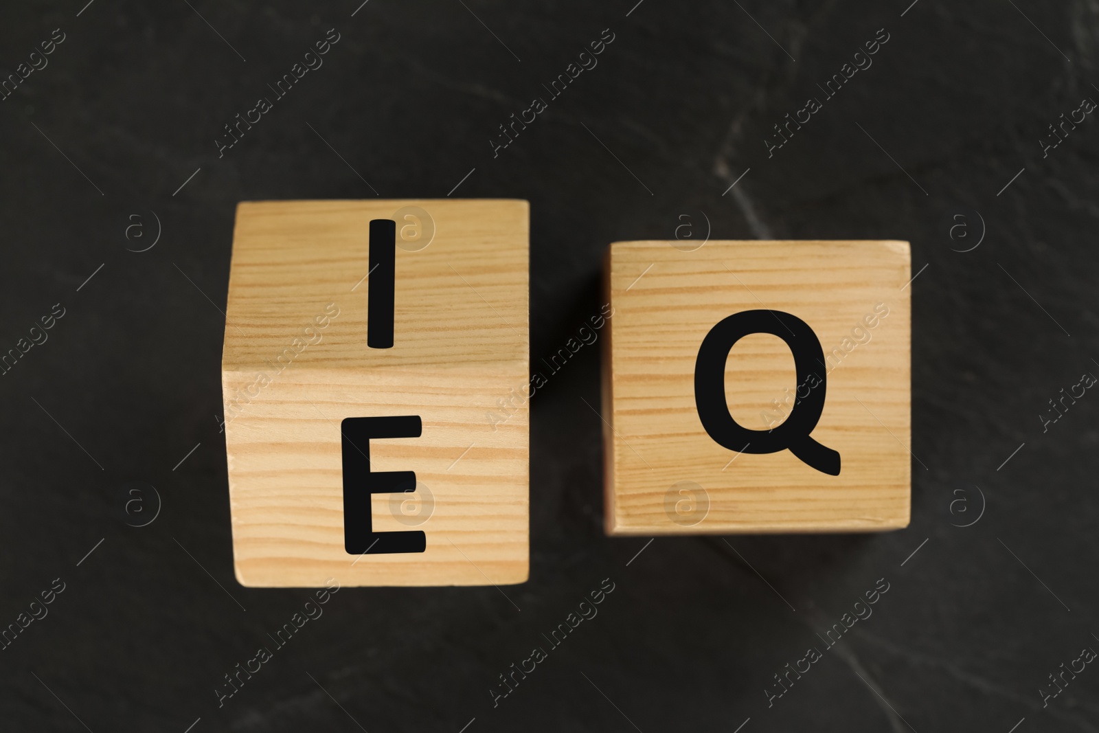 Photo of Wooden cubes with letters E, I and Q on black slate background, flat lay