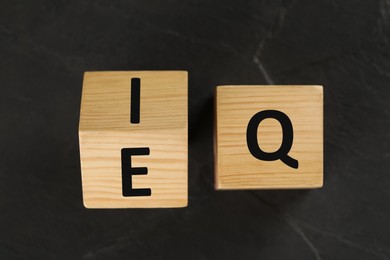 Photo of Wooden cubes with letters E, I and Q on black slate background, flat lay
