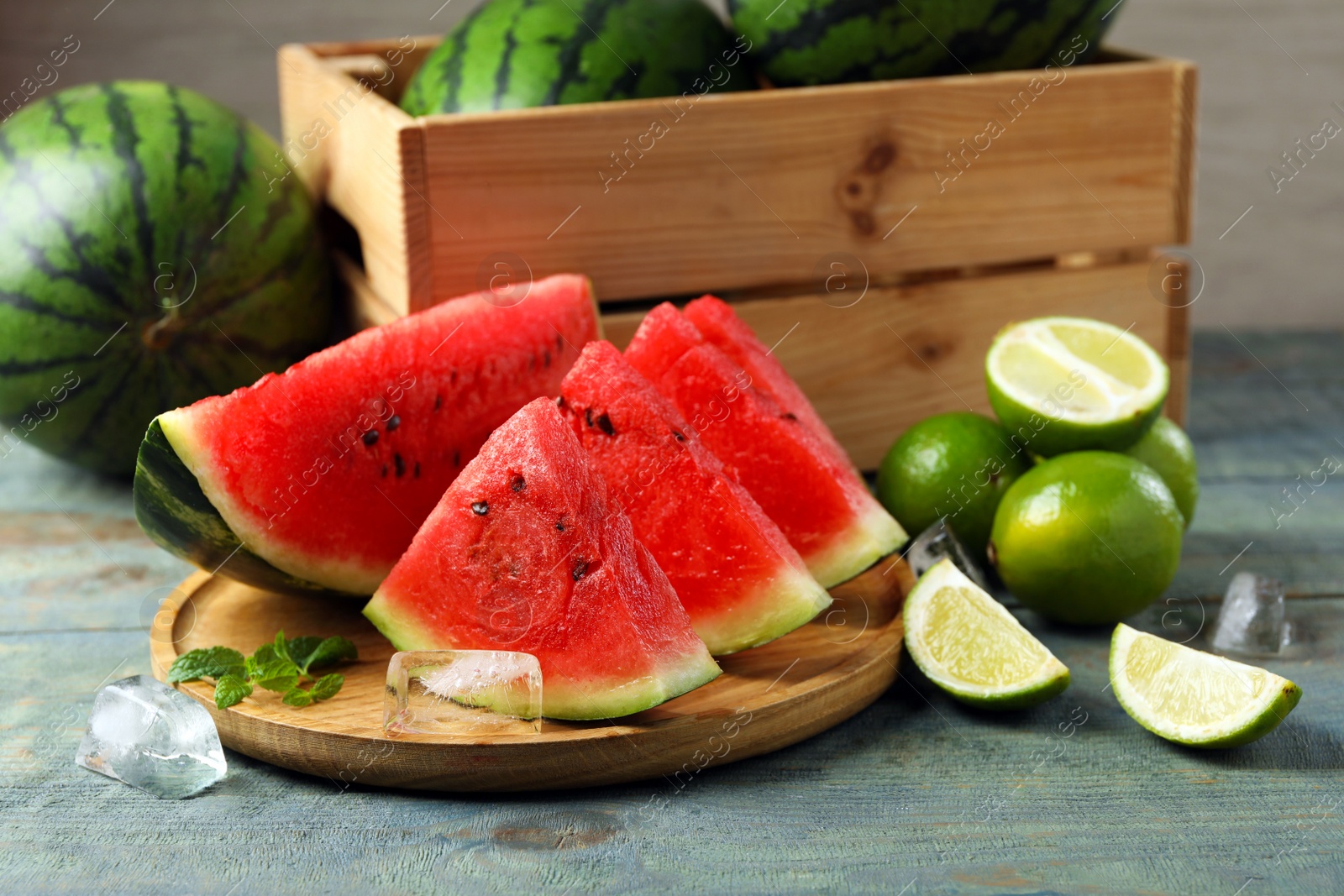 Photo of Slices of delicious watermelon, limes, ice and mint on light blue wooden table