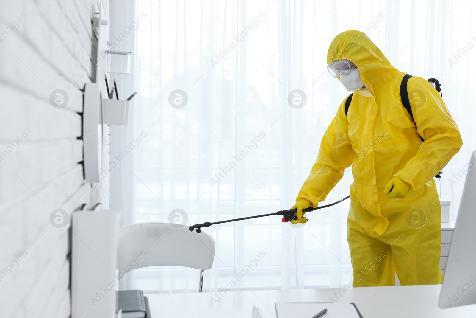 Photo of Employee in protective suit sanitizing office. Medical disinfection