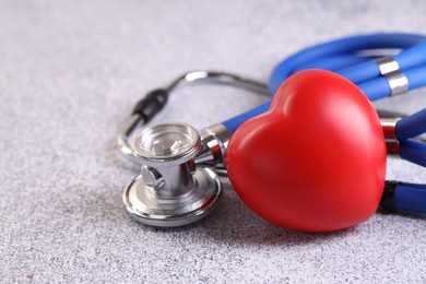 Photo of Stethoscope and red heart on grey stone table, closeup. Space for text