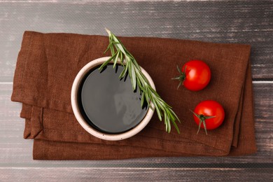 Photo of Bowl with balsamic vinegar, rosemary and tomatoes on wooden table, flat lay