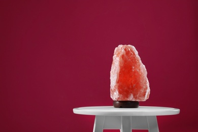 Photo of Himalayan salt lamp on white table against dark pink background, space for text