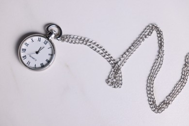 Silver pocket clock with chain on light table, top view