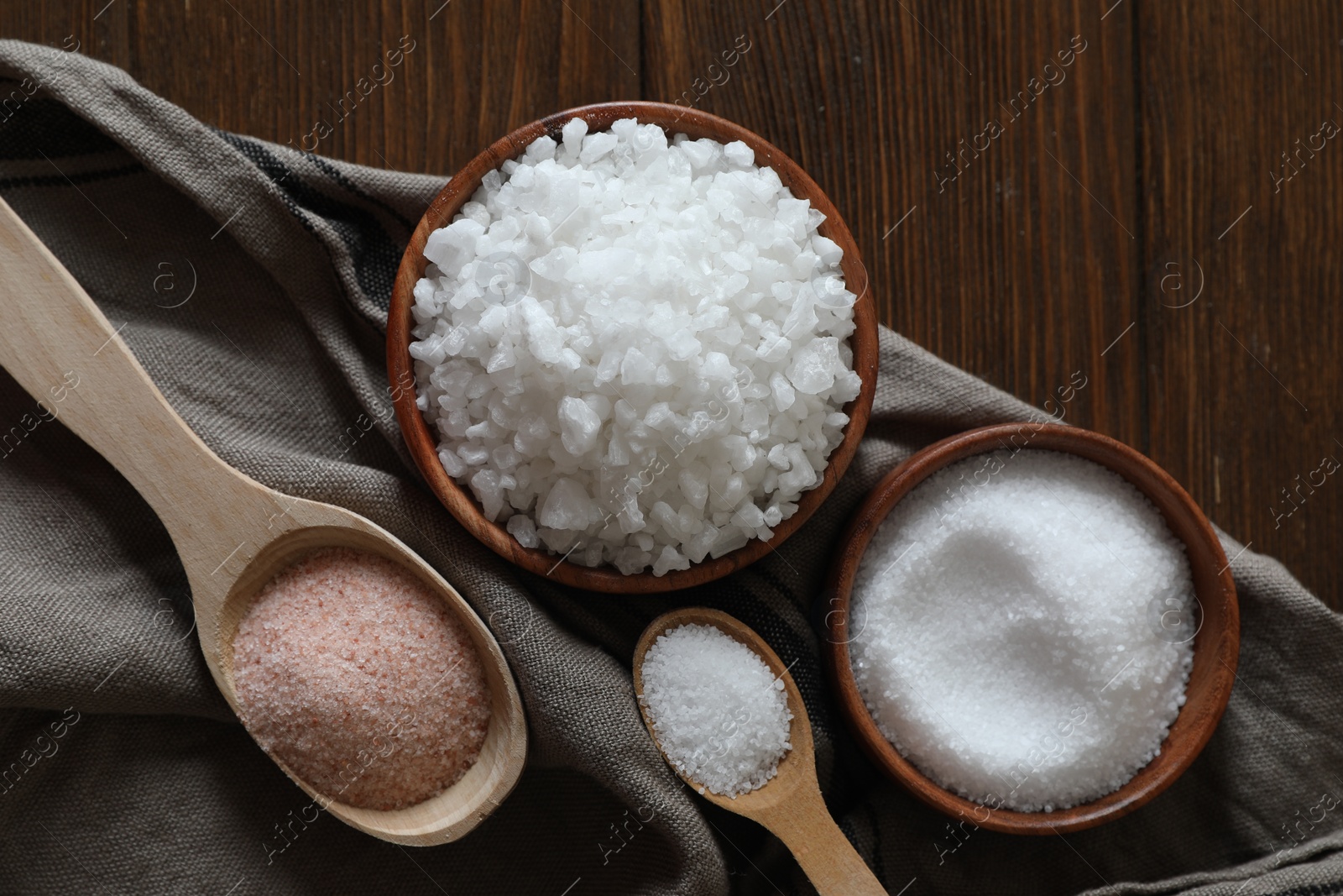 Photo of Different types of organic salt on wooden table, flat lay