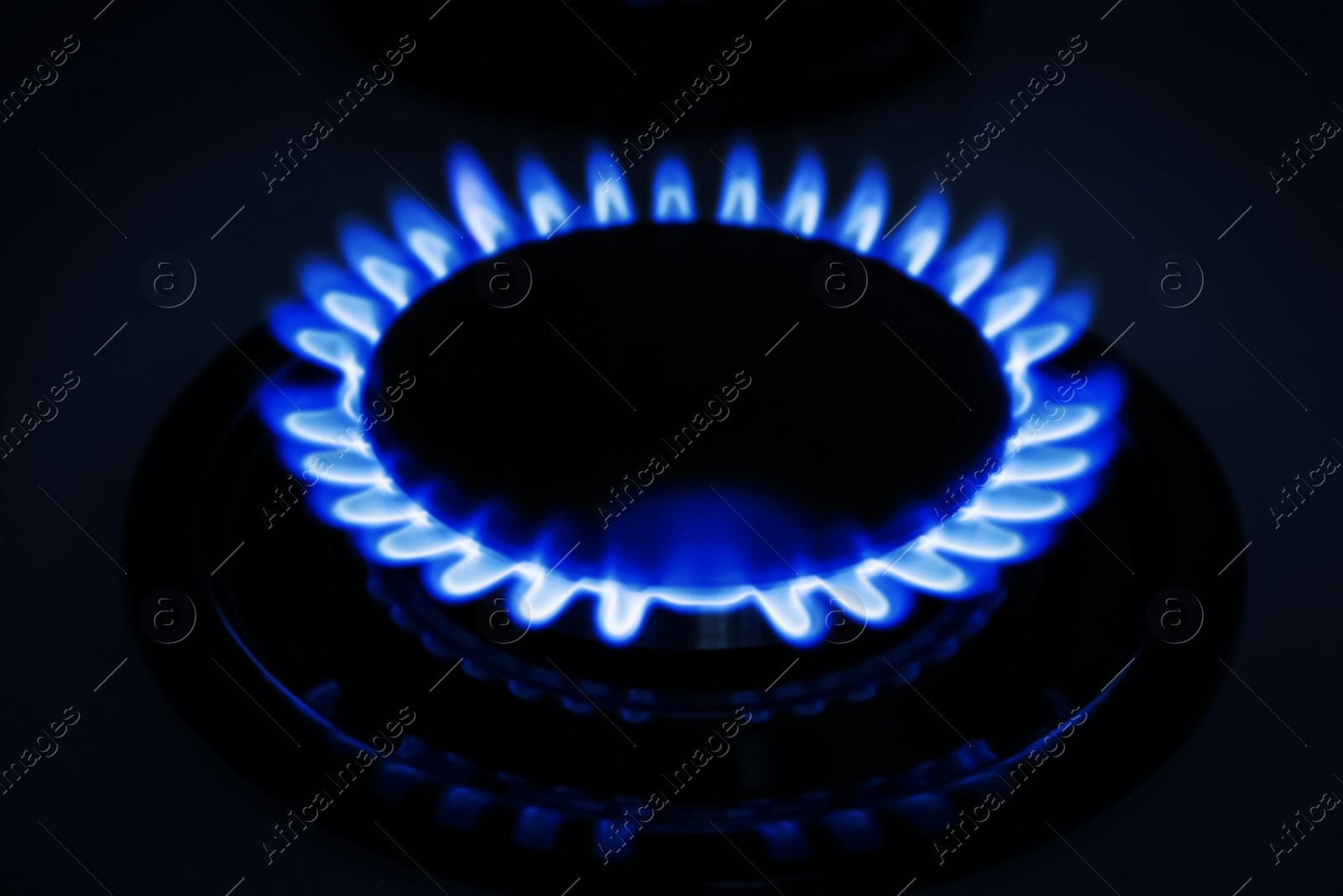 Photo of Gas burner of modern stove with burning blue flame at night, closeup