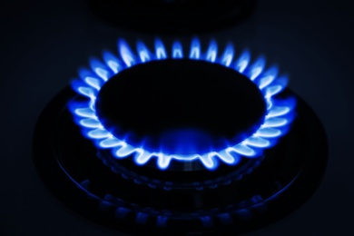Photo of Gas burner of modern stove with burning blue flame at night, closeup