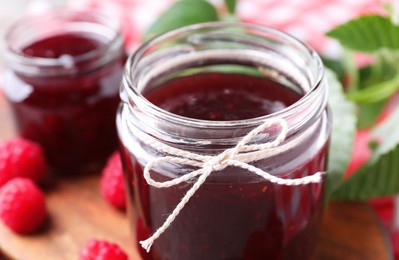 Photo of Glass jar of delicious raspberry jam on board, closeup