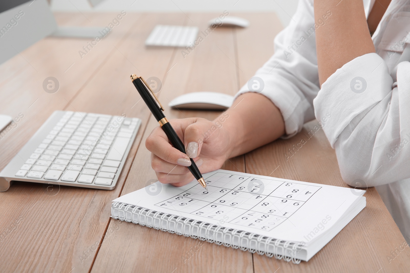 Photo of Woman solving sudoku puzzle at table, closeup