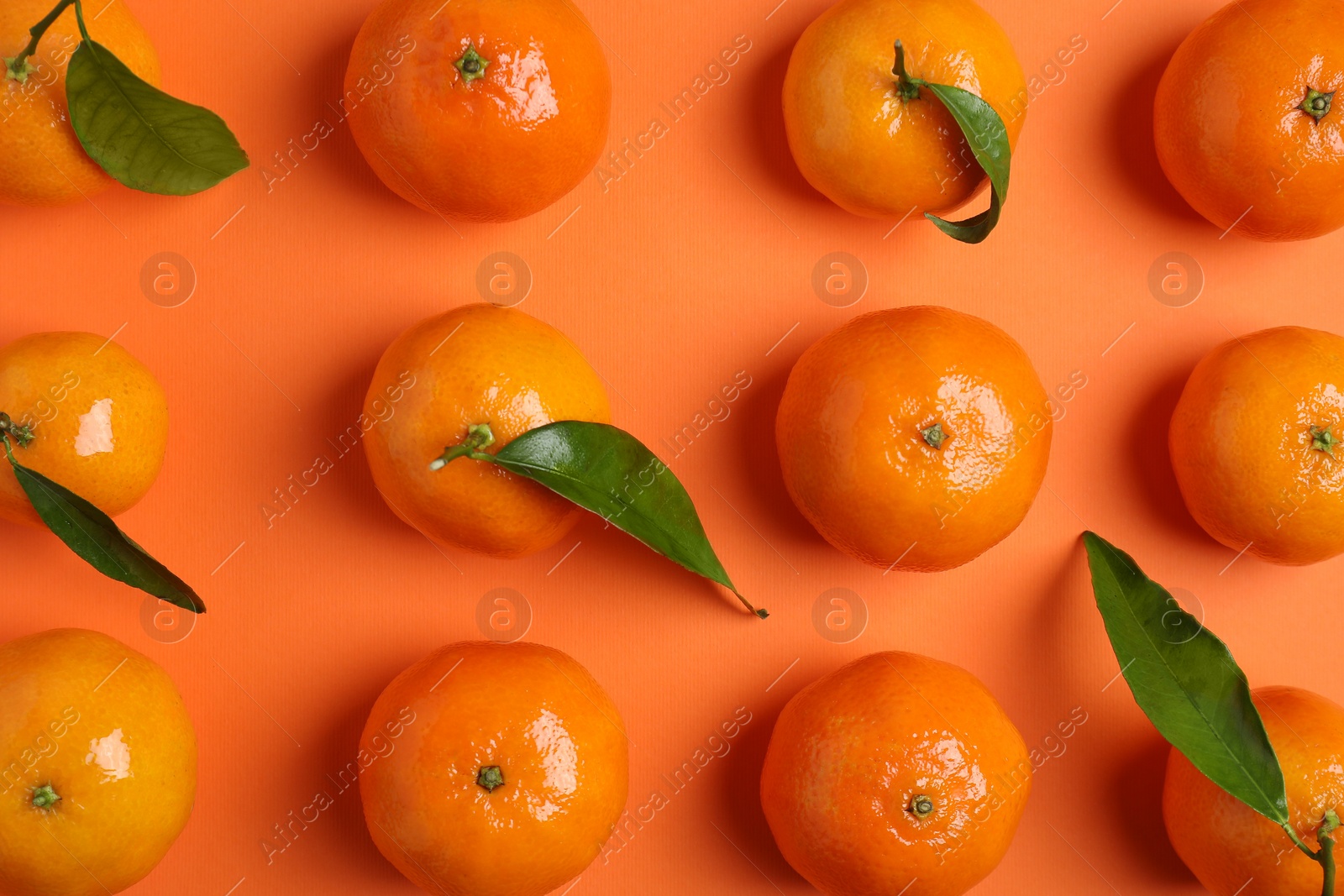 Photo of Delicious tangerines with green leaves on orange background, flat lay