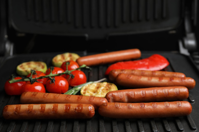 Photo of Cooking delicious fresh sausages with vegetables on modern grill