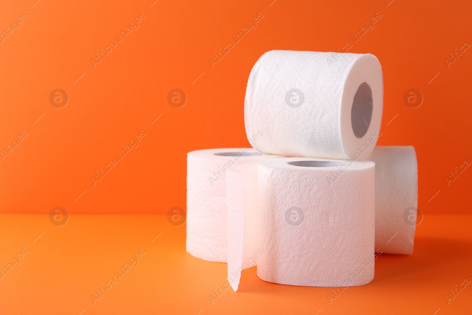 Photo of Soft toilet paper rolls on orange background, closeup. Space for text