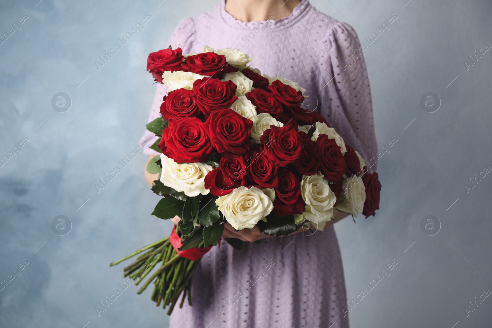 Photo of Woman holding luxury bouquet of fresh roses on light blue background, closeup