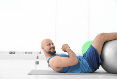 Overweight man doing exercise with fitness ball in gym