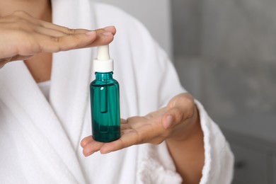 Photo of Woman with bottle of cosmetic serum on blurred background, closeup