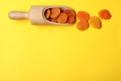 Photo of Wooden scoop of dried apricots on color background, top view with space for text. Healthy fruit
