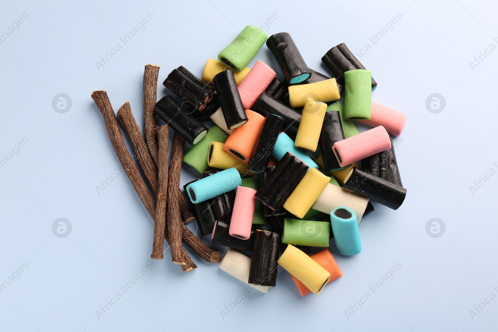 Photo of Tasty candies and dried cut liquorice root on light blue background, top view