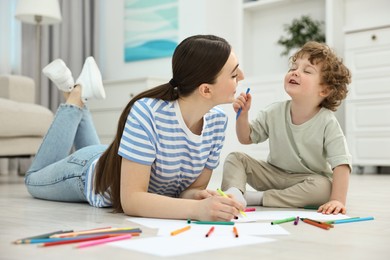 Photo of Mother and her little son drawing with colorful markers on floor at home