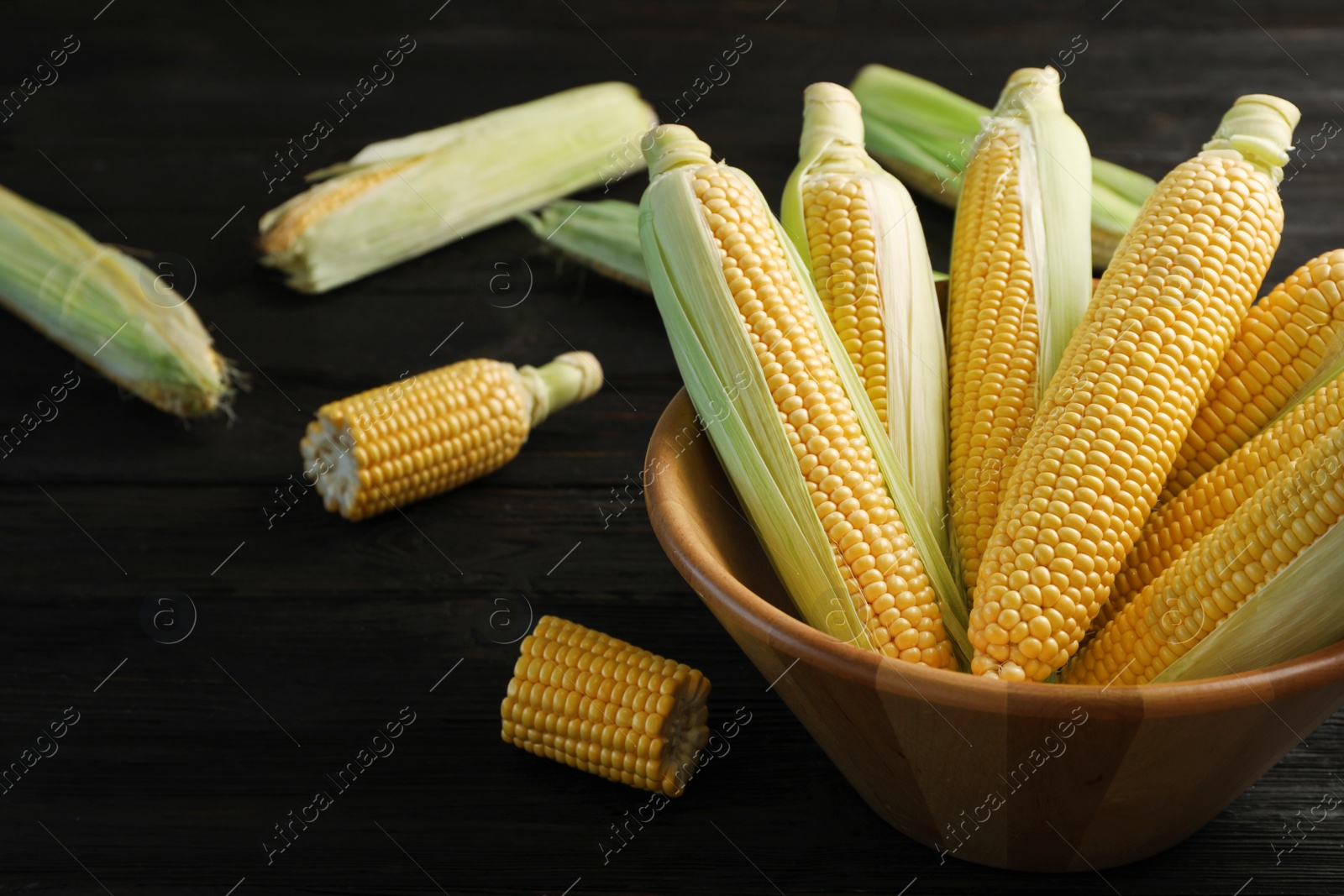 Photo of Bowl with tasty sweet corn cobs on table, closeup