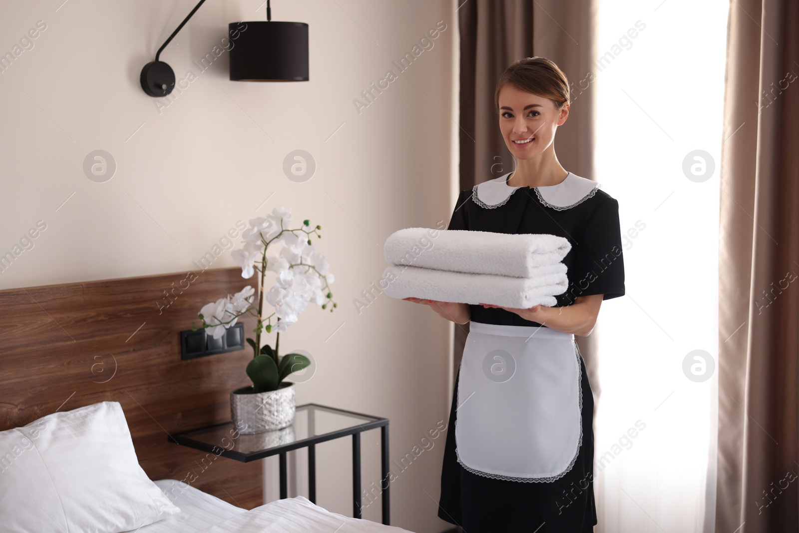 Photo of Beautiful chambermaid with stack of fresh towels in hotel room