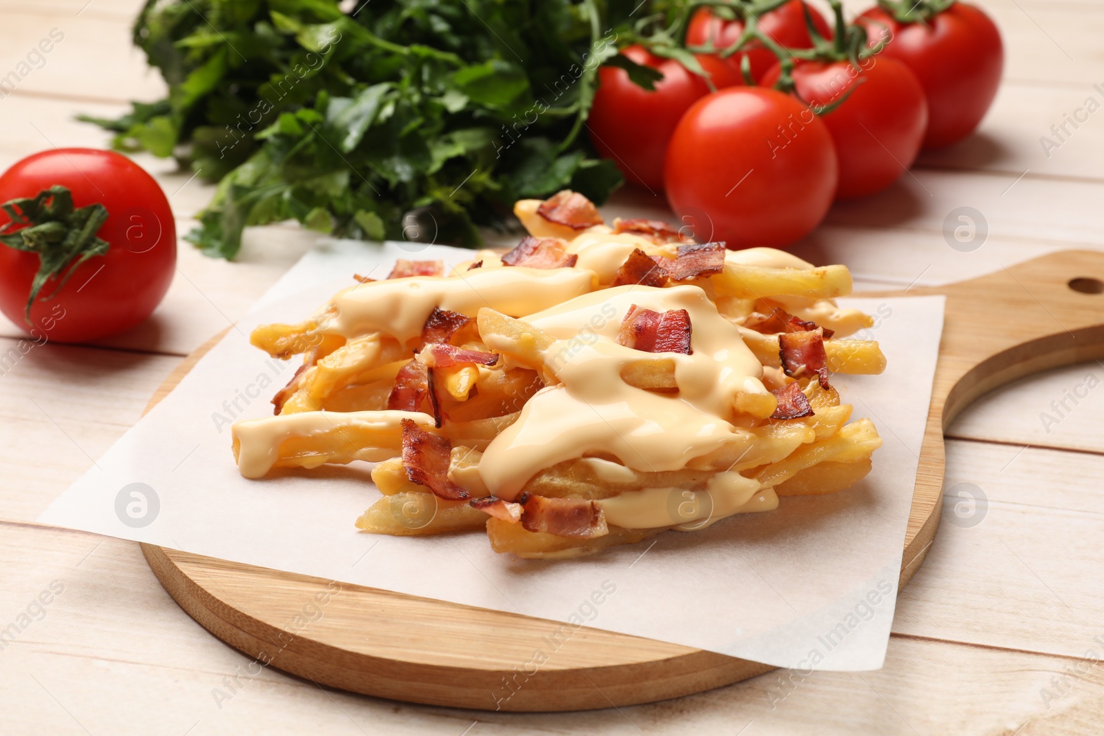 Photo of Delicious French fries with bacon, cheese sauce, tomatoes and herbs on wooden table, closeup