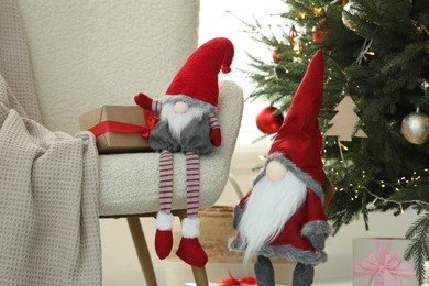 Funny decorative gnomes with gift boxes near Christmas tree indoors
