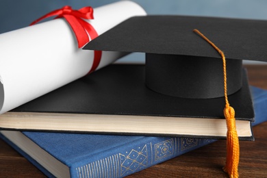 Graduation hat, books and student's diploma on wooden table, closeup