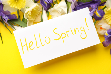Photo of Card with words HELLO SPRING and fresh flowers on yellow background, flat lay