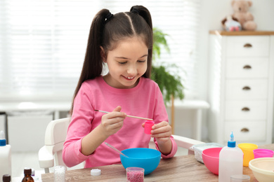 Photo of Cute little girl making homemade slime toy at table indoors