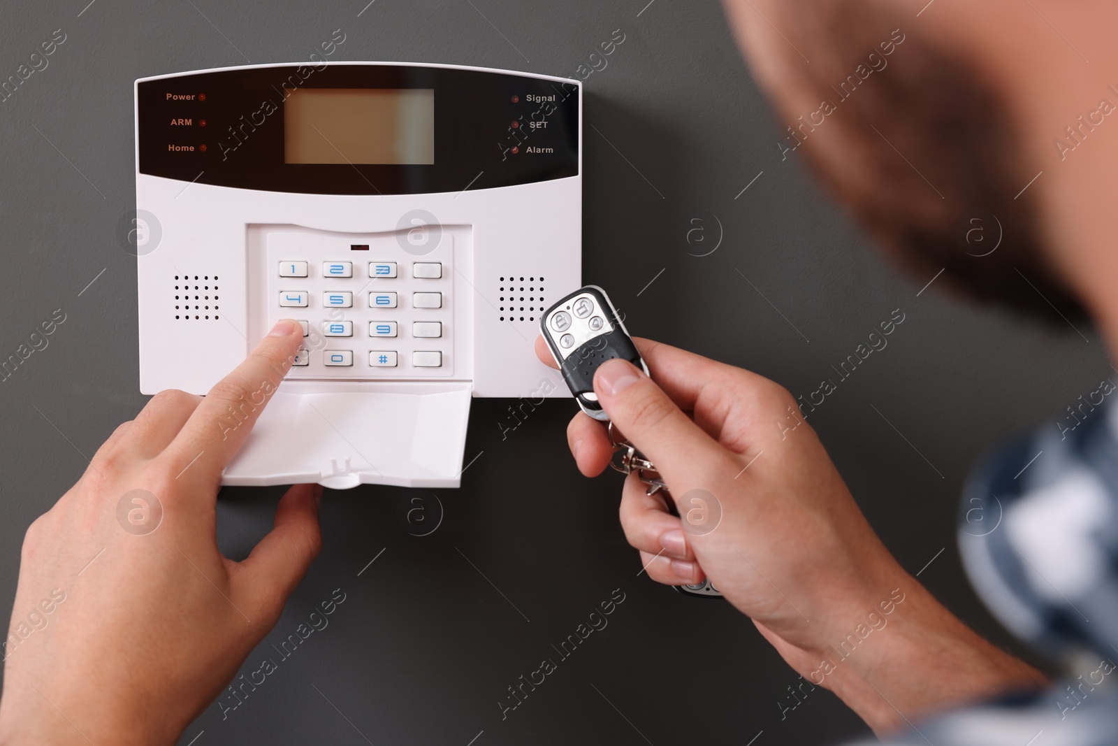 Photo of Man checking home security alarm system with key fob near gray wall, closeup