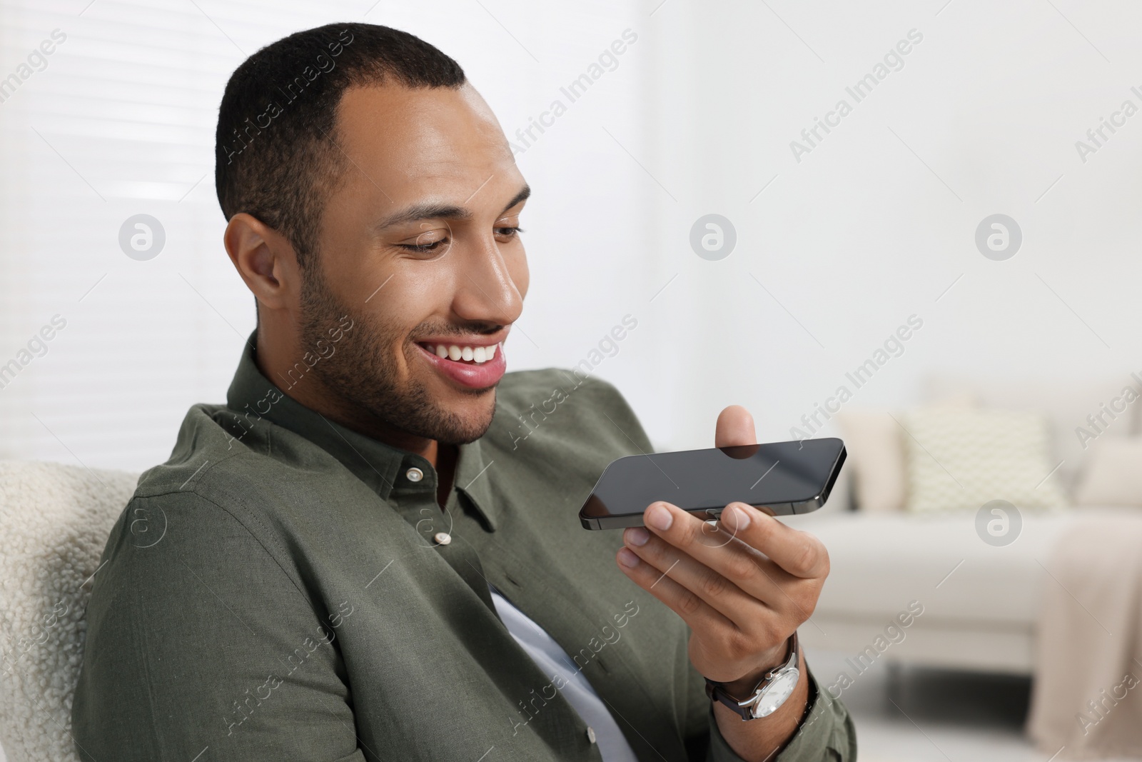 Photo of Happy man sending voice message via smartphone indoors