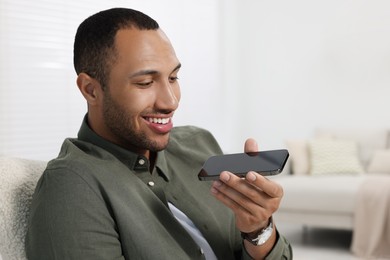 Happy man sending voice message via smartphone indoors