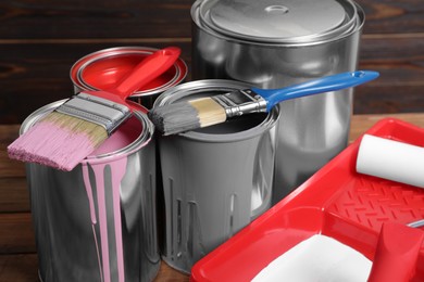 Photo of Cans of paints, brushes and tray with roller on wooden table, closeup