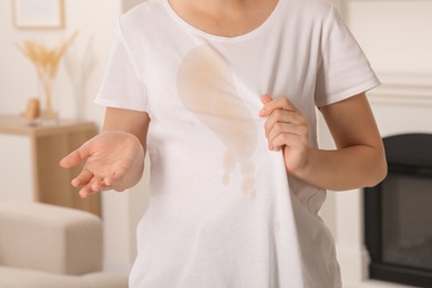Photo of Woman showing stain from coffee on her shirt indoors, closeup