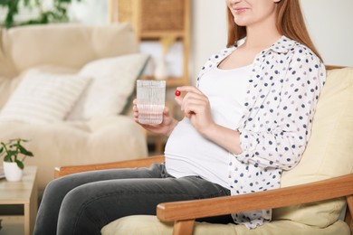 Photo of Pregnant woman holding pill and glass of water at home, closeup