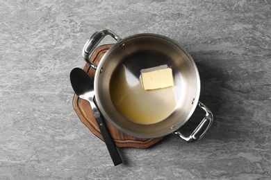 Pot with melting butter and spoon on grey background, top view