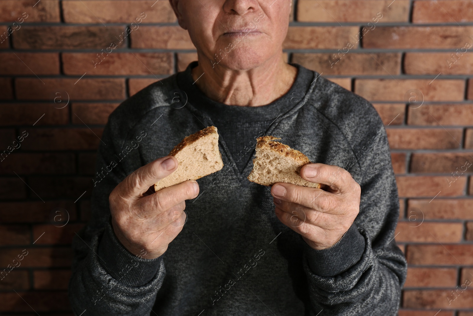 Photo of Poor elderly man with bread near brick wall, closeup