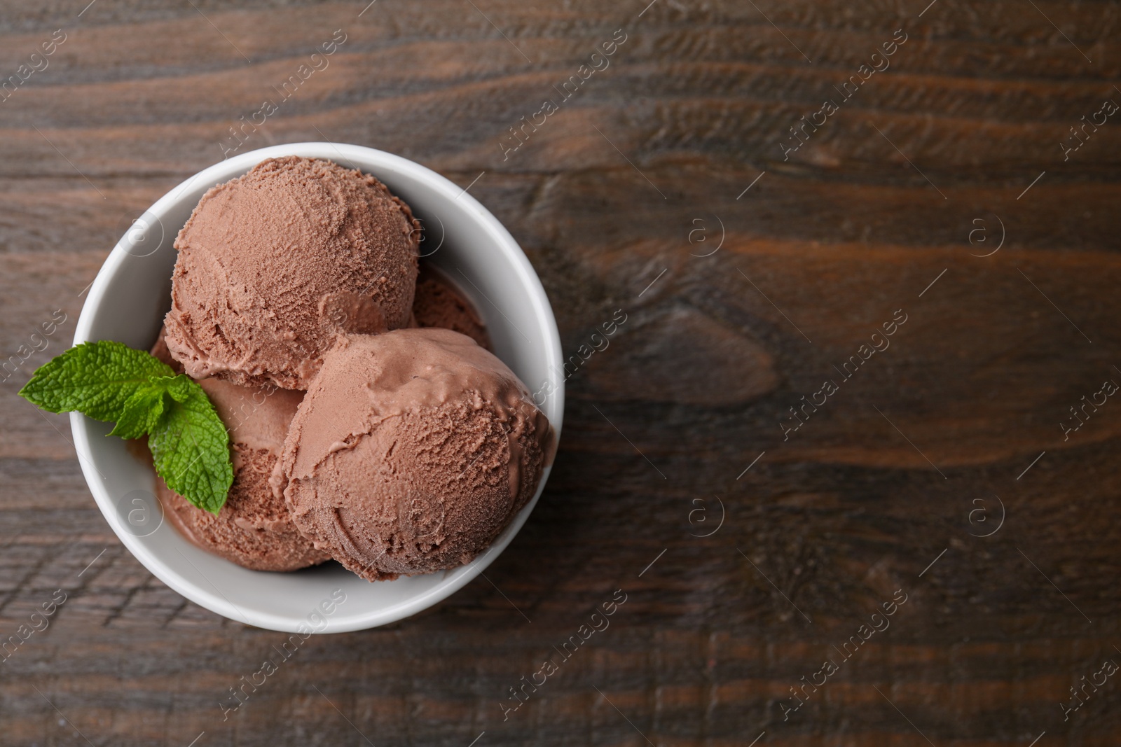 Photo of Bowl with tasty chocolate ice cream and mint leaves on wooden table, top view. Space for text