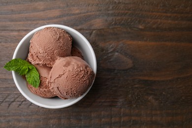 Bowl with tasty chocolate ice cream and mint leaves on wooden table, top view. Space for text