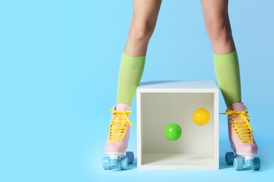 Photo of Woman wearing vintage roller skates near storage cube with balls on color background, closeup. Space for text