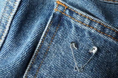 Metal safety pins on denim fabric, closeup