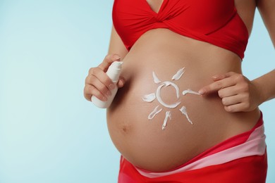Photo of Young pregnant woman with sun protection cream on light blue background, closeup. Space for text
