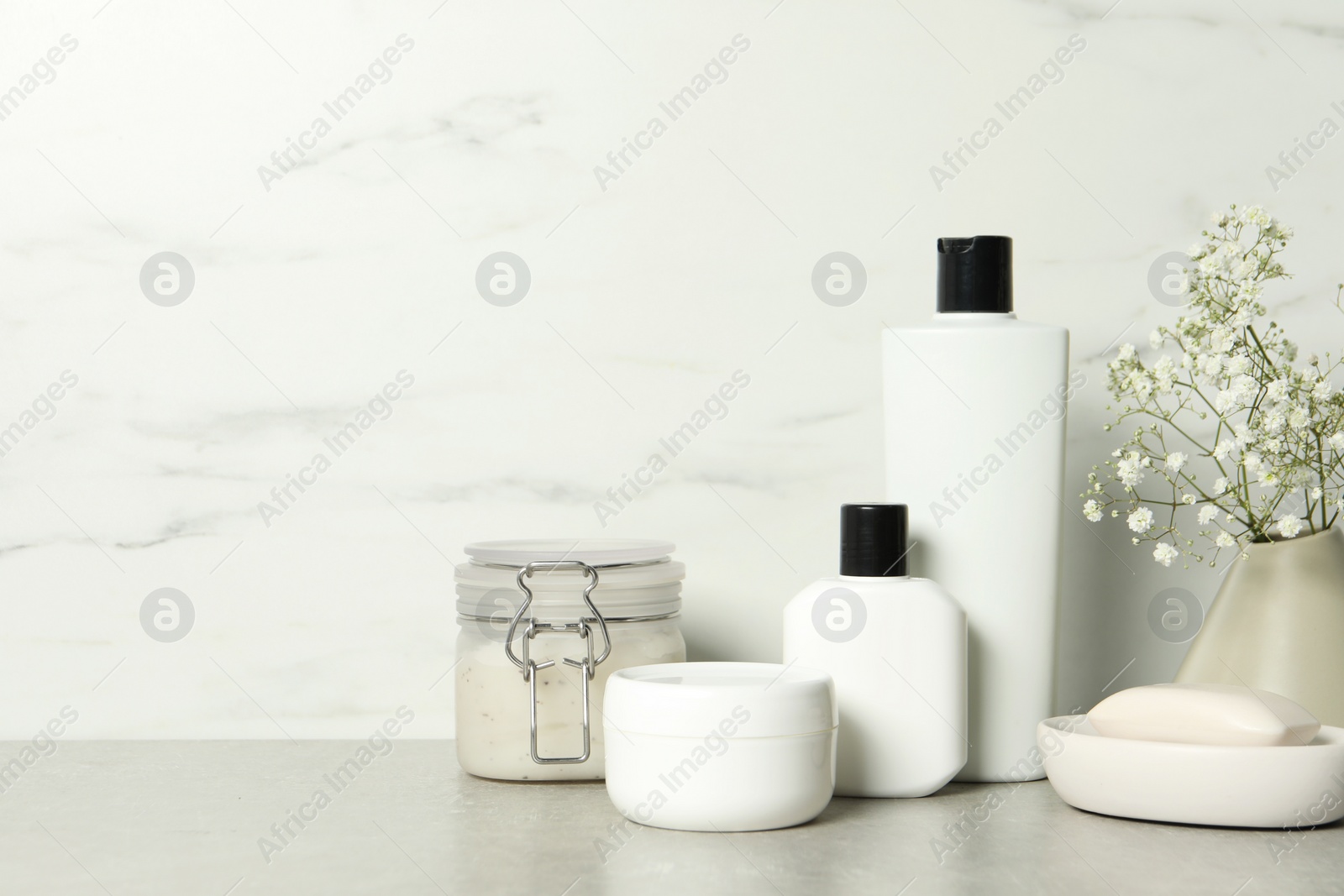 Photo of Bath accessories. Personal care products and gypsophila flowers in vase on gray table near white marble wall, space for text