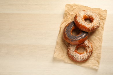 Many delicious fresh bagels on light wooden table, top view. Space for text