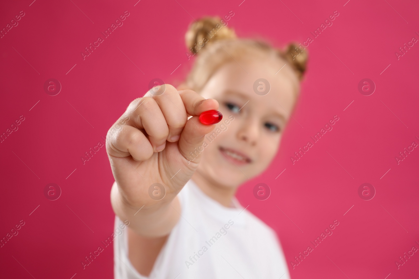 Photo of Little girl with vitamin pill against pink background, focus on hand