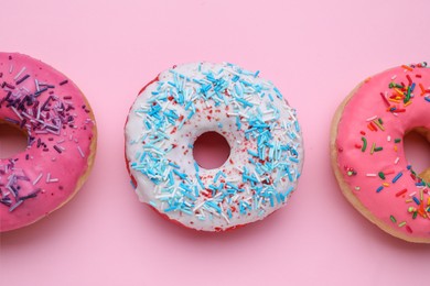 Photo of Glazed donuts decorated with sprinkles on pink background, flat lay. Tasty confectionery