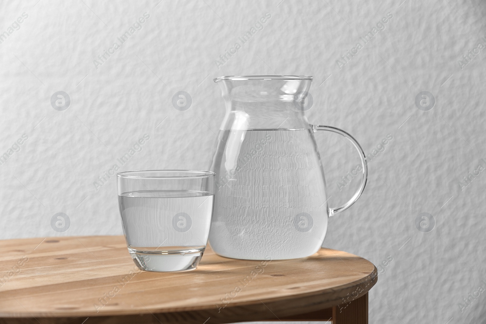 Photo of Pitcher and glass with water on table near white wall