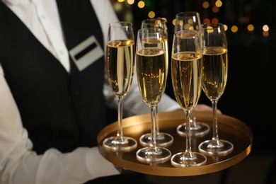 Waiter holding tray with glasses of champagne on blurred background, closeup