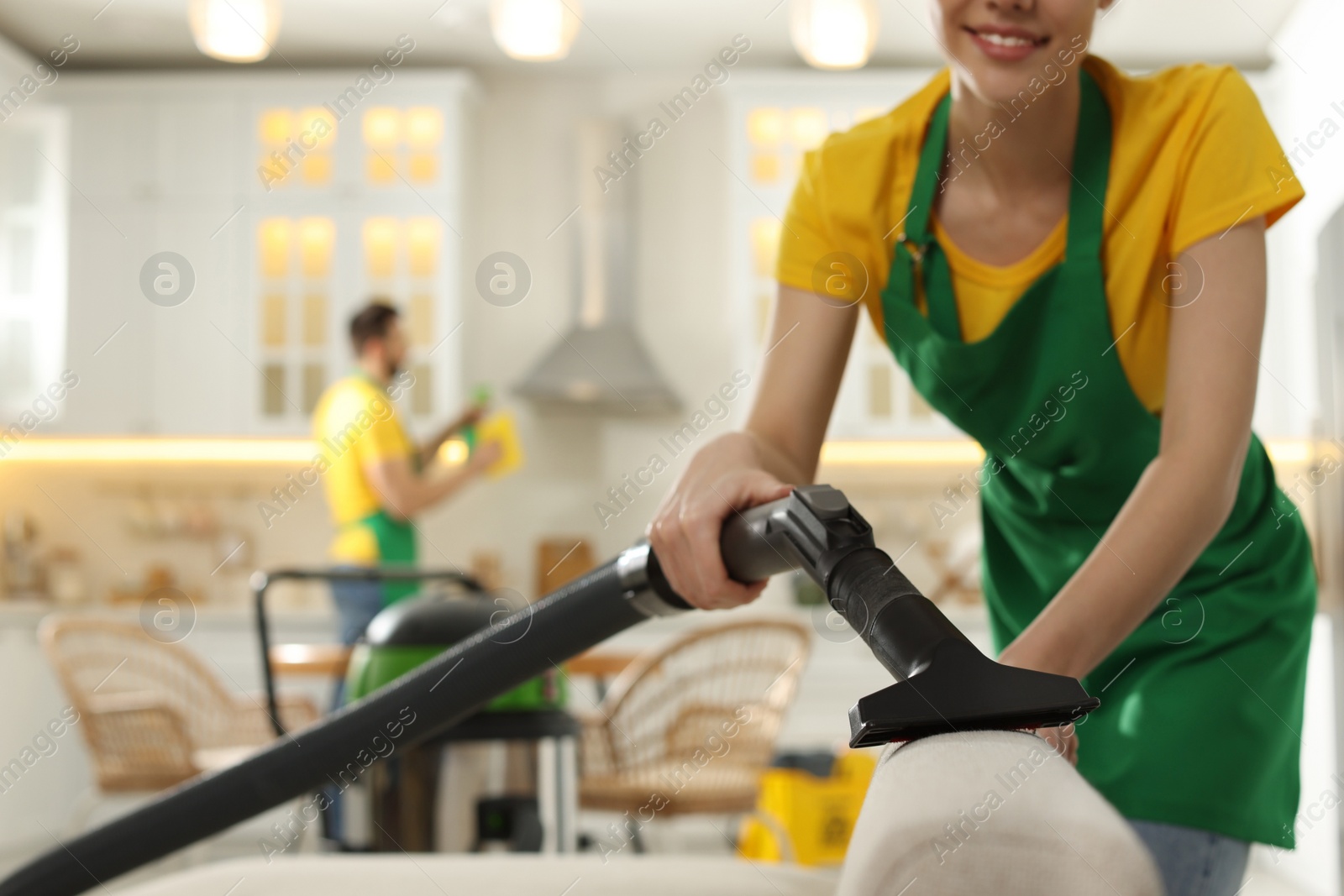 Photo of Professional janitor in uniform vacuuming sofa indoors, closeup. Space for text